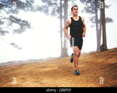 Einfach weiter in Bewegung. Ein sportlicher junger Mann, der auf einen Lauf im Wald aus ist. Stockfoto