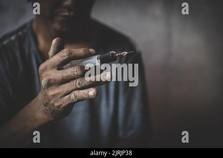 Drogenabhängiger Mann mit Spritze, der Drogen verwendet. Drogenkonzept. Dunkles Thema, junger Mann sehr gestresst, Er würde Drogenabhängigkeit. Stockfoto