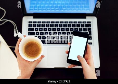 Multitasking wie ein Chef. Aufnahme einer nicht identifizierbaren Frau, die ihr Telefon und ihren Laptop benutzt, während sie eine Tasse Kaffee trinkt. Stockfoto