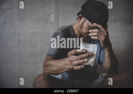 Das süchtig machende Konzept eines Mannes, der sitzt und seine Herointasche trägt. Selbstzerstörerische Depression, Drogenabhängigkeit, Selbstmord, Drogenabhängigkeit. Stockfoto