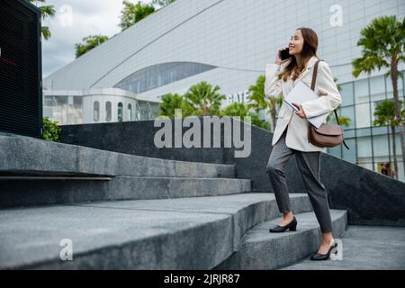 Die Geschäftsfrau, die in der Stadt die Treppe hoch stieg, hielt einen Laptop und sprach ein Mobiltelefon. Sie beeilte sich, die Treppe zu betreten, zur Hauptverkehrszeit, um im Büro zu arbeiten Stockfoto