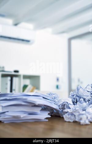 Jemand muss sich mit einigen Papierkram aufholen. Ein Haufen zusammengeknitterter Papierkram sitzt auf einem Schreibtisch. Stockfoto