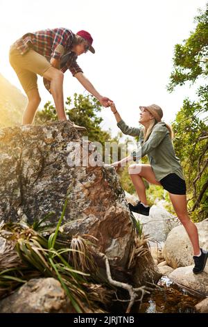Nichts ganz so motivierendes wie die Liebe. Ein junger Mann hilft seiner Freundin, einen Felsen in der Natur zu erklimmen. Stockfoto