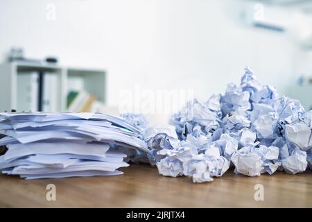 Papierkram häufen sich. Ein Haufen zusammengeknüllter Papierkram sitzt auf einem Schreibtisch. Stockfoto