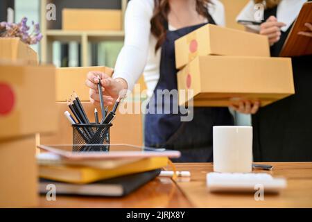 Zwei weibliche Kleinunternehmer arbeiten im Lagerraum zusammen und bereiten ihre Versandkartons vor, um sie an einen Postlieferdienst zu schicken. c Stockfoto