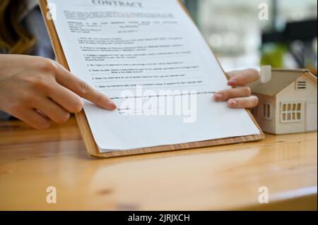 Nahaufnahme, Eine Immobilienmaklerin, die das Dokument zum Vertrag über die Immobilieninvestition zeigt, und die Unterschrift, um den Deal abzuschließen. Stockfoto