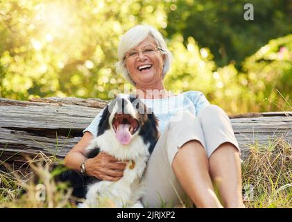 Manche Engel haben Pelz anstelle von Flügeln. Porträt einer glücklichen älteren Frau, die sich mit ihrem Hund in einem Park entspannt. Stockfoto