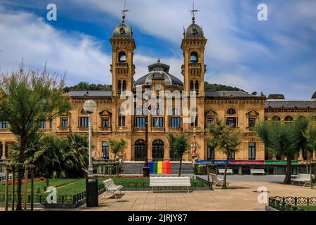 San Sebastian, Spanien - 26 2021. Juni: Prunkvolle Rathausfassade im Alderdi Eder Gardens Park mit einer LGBT-Stolz-Regenbogenflagge auf der vorderen Treppe Stockfoto
