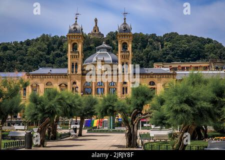 San Sebastian, Spanien - 26 2021. Juni: Prunkvolle Rathausfassade im Alderdi Eder Gardens Park mit einer LGBT-Stolz-Regenbogenflagge auf der vorderen Treppe Stockfoto