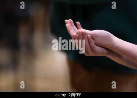 Die Hände des Pfarrers, die zusammengekrallt sind, um den Wirt oder das Brot vom Priester bei der katholischen Messe oder der Kommunionliturgie oder der Messe zu empfangen. Stockfoto