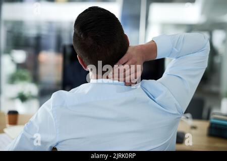 Das tut wirklich weh. Rückansicht eines jungen Geschäftsmannes, der während der Arbeit in einem Büro Nackenschmerzen hatte. Stockfoto