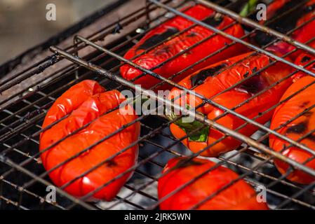Grillen Prozess der Vorbereitung roten Paprika auf Grill bbq Grill. Flammendes Feuer, Kohle und Rauch. Nahaufnahme der ganzen Straße Food Picknick vegetab Stockfoto