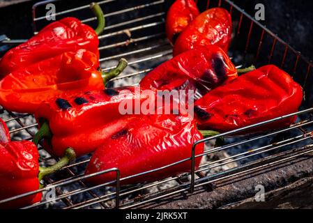Grillen Prozess der Vorbereitung roten Paprika auf Grill bbq Grill. Flammendes Feuer, Kohle und Rauch. Nahaufnahme der ganzen Straße Food Picknick vegetab Stockfoto