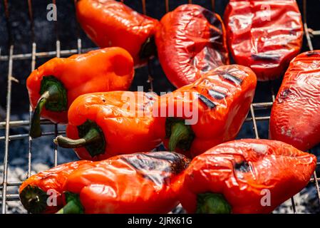 Grillen Prozess der Vorbereitung roten Paprika auf Grill bbq Grill. Flammendes Feuer, Kohle und Rauch. Nahaufnahme der ganzen Straße Food Picknick vegetab Stockfoto