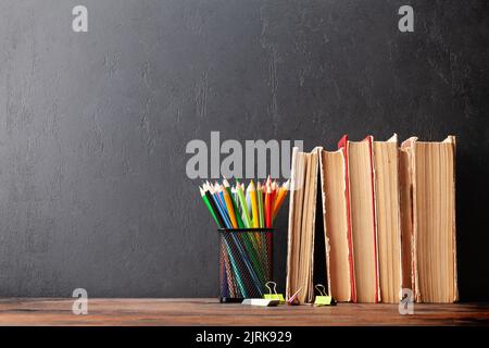 Alte Bücher und Bleistifte auf Holztisch vor Tafel mit Kopierplatz Stockfoto
