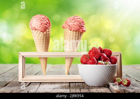 Erdbeereis in Waffelkonen und Schale mit Beeren auf dem Gartentisch Stockfoto
