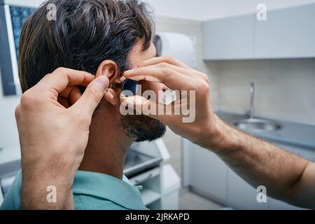 HNO, der in seiner Klinik eine professionelle Untersuchung des Ohrs eines männlichen Patienten durchgeführt hat. Ohren-Check-up, Nahaufnahme Stockfoto