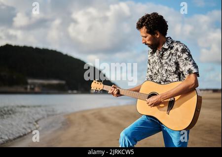 Seitenansicht eines männlichen Musikers, der an sonnigen Tagen am Strand akustische Gitarre spielt Stockfoto