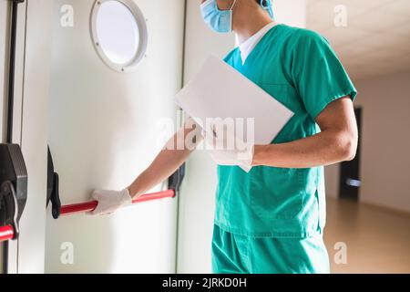 Crop anonymen männlichen Sanitäter in steriler Maske und Handschuhe öffnen Tür mit Fenster im Krankenhaus Durchgang Stockfoto