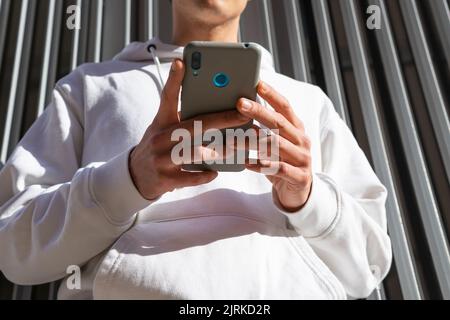 Von unten beschnitten unerkennbarer Mann, der in der Nähe einer Metallwand in der Stadt stand und über das Mobiltelefon in den sozialen Medien Nachrichten aussagte Stockfoto