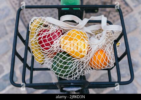 Von oben umweltfreundliche Netztasche mit frischem Obst und Gemüse in Metallkorb mit Fahrrad auf der Straße in der Stadt geparkt platziert Stockfoto