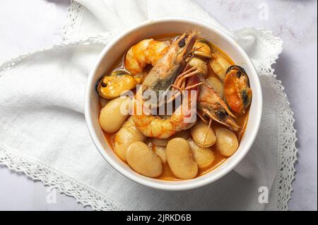 Von oben Schale mit typischem Eintopf aus Bohnen mit Garnelen, Garnelen und Muscheln auf einer Spitzentischdecke und auf einem Steintisch Stockfoto