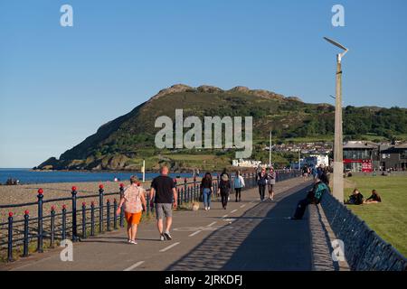 Menschen, die an einem sonnigen Sommertag entlang der Strandpromenade in Bray, Co. Wicklow, Irland, spazieren gehen. Der Bray Head Berg im Hintergrund. Stockfoto