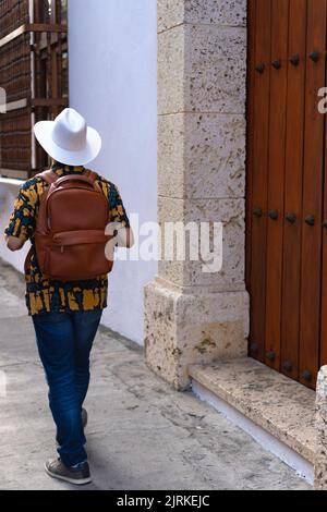 Anonymer männlicher Tourist mit Hut und Rucksack, der am Sommertag auf der Straße in der Nähe des Gebäudes unterwegs ist Stockfoto