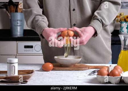 Crop unkenntlich männlichen Koch brechen Ei in Schüssel, während köstliche spanische Omelette am Tisch zu Hause zubereiten Stockfoto