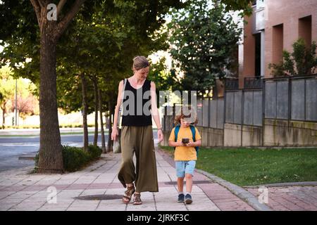 Mutter und Sohn gehen nach der Schule die Straße entlang. Stockfoto