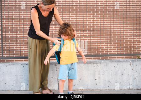 Mutter, die den Rucksack ihres Kindes anzieht, bevor sie zur Schule geht. Stockfoto