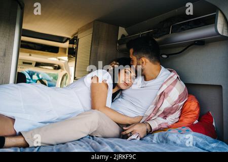 Zartes, hispanisch Reisender Paar, das sich auf dem Bett entspannt und im Wohnwagen kuschelt, während er die Reise genießt Stockfoto