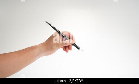 Die Hand eines Mannes hält eine Kalligraphie und einen Schreibstift in seiner linken Hand auf einem weißen Hintergrund. Hochwertige Fotos Stockfoto