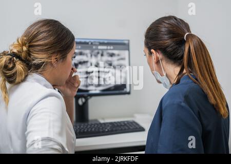 Rückansicht von Frauen in medizinischen Uniform diskutieren Zähne Röntgen auf Computer-Monitor während der Arbeit im Labor der zeitgenössischen Zahnklinik Stockfoto