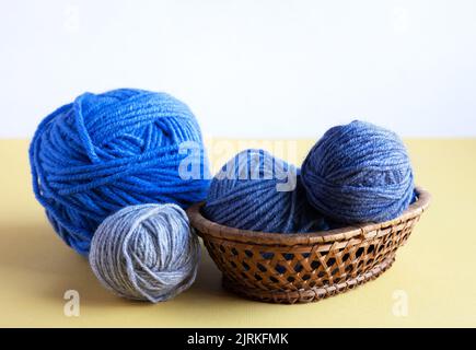 Blaue Strickgarnkugeln auf gelbem Hintergrund in einem Korb Stockfoto