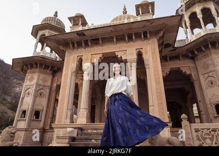 Von unten fröhliche asiatische Frau lächelnd und Blick auf die Kamera, während in der Nähe von gealterten Gaitor Ki Chhatriyan Gebäude in Jaipur, Indien Stockfoto