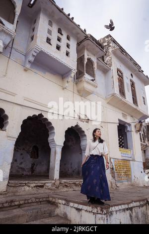 Niedriger Winkel der ethnischen Frau steht gegen verwitterte alte Gebäude am Ufer des Heiligen Sees Pushkar in Rajasthan, Indien Stockfoto