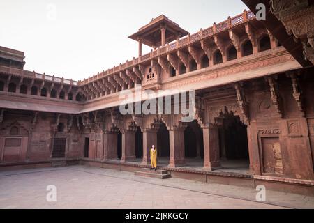 Ethnische asiatische Frau, die in gelbem Kleid in einem alten gewölbten Agra Fort in Uttar Pradesh, Indien, wegschaut Stockfoto