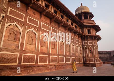 Ganzkörperfrau, die in gelbem Kleid wegschaut und im gealterten Agra Fort in Uttar Pradesh, Indien, steht Stockfoto