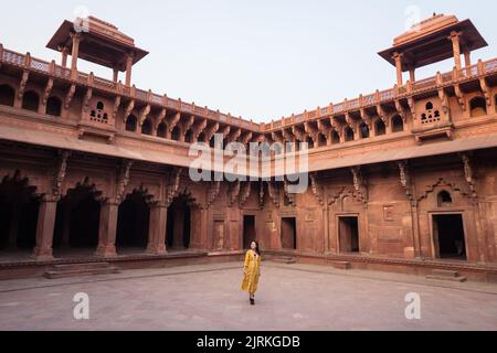 Ethnische asiatische Frau, die in gelbem Kleid in einem alten gewölbten Agra Fort in Uttar Pradesh, Indien, wegschaut Stockfoto