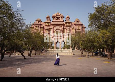 Rückansicht einer anonymen Reisenden, die am sonnigen Tag in Jaipur, Indien, auf dem Bürgersteig in Richtung eines alten Patrika Gate-Gebäudes geht Stockfoto