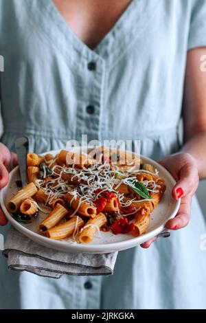 Nahaufnahme einer zugeschnittenen Frau, die einen Teller mit köstlicher Pasta alla Puttanesca hält Stockfoto