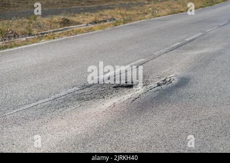 Deformierte Asphaltoberfläche mit Schlaglöchern, die durch schwere überlastete Lkw auf der Autobahn verursacht werden Stockfoto