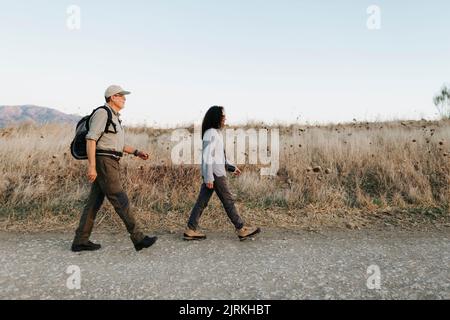 Ganzkörper-Seitenansicht eines reifen Paares in legerer Kleidung, das auf einer Wiese auf dem Land läuft Stockfoto
