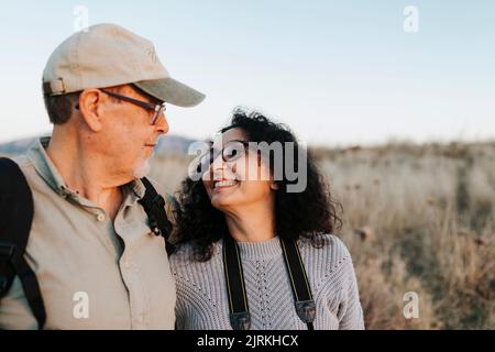 Fröhliches reifes Paar in lässiger Kleidung, umarmt und stehend auf einer Wiese auf dem Land Stockfoto