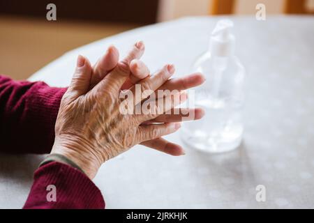 Hoher Winkel von anonymen älteren Menschen, die sich zu Hause mit Desinfektionsmittel die Hände über den Tisch klatschen Stockfoto
