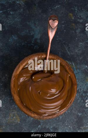 Draufsicht auf einen Dulce de leche in brauner Schüssel gemischt mit einem Löffel auf schwarzem Hintergrund Stockfoto