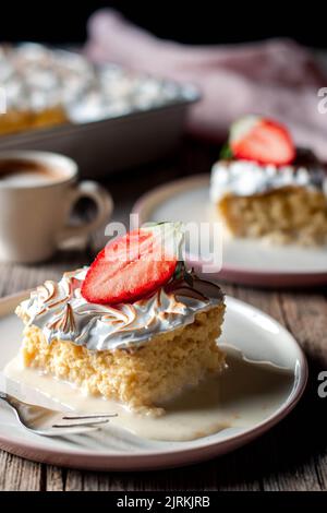 Süßer, köstlicher Kuchen aus drei Milchsorten mit halbfrischer Erdbeere auf weißem Teller auf Holztisch Stockfoto