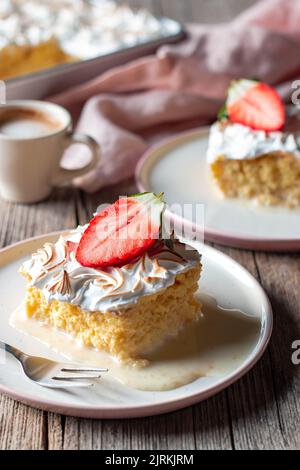 Süßer, köstlicher Kuchen aus drei Milchsorten mit halbfrischer Erdbeere auf weißem Teller auf Holztisch Stockfoto