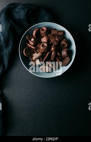 Draufsicht auf verschiedene dunkle Schokoladentrüffel und Pralinen in verschiedenen Formen in einer Schüssel auf einem schwarzen Tisch Stockfoto
